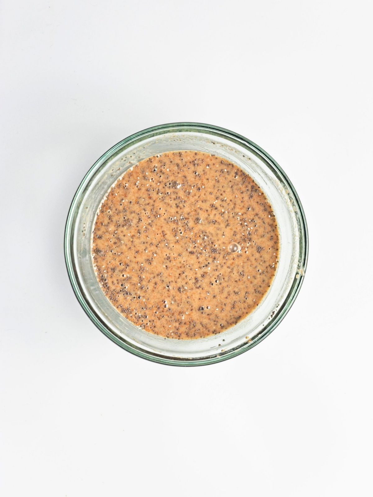 Cinnamon-colored oatmeal batter with chia seeds mixed into a glass bowl for vegan baked apple protein oatmeal, ready for the remaining ingredients before baking.
