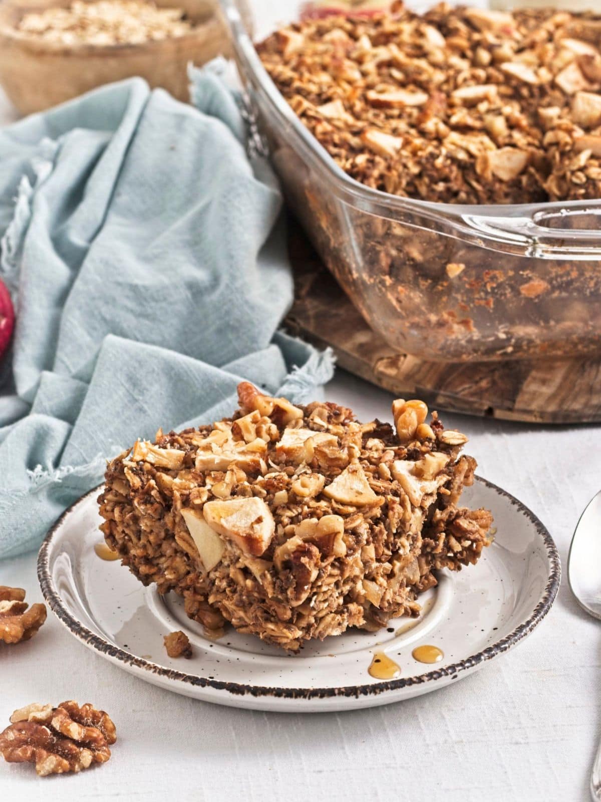A slice of Vegan of baked apple protein oatmeal on a plate filled with rolled oats, chopped apples, walnuts, and warm cinnamon. 