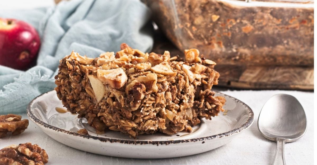 Close up image of a slice vegan apple protein oatmeal with sliced apples on top in a baking dish.