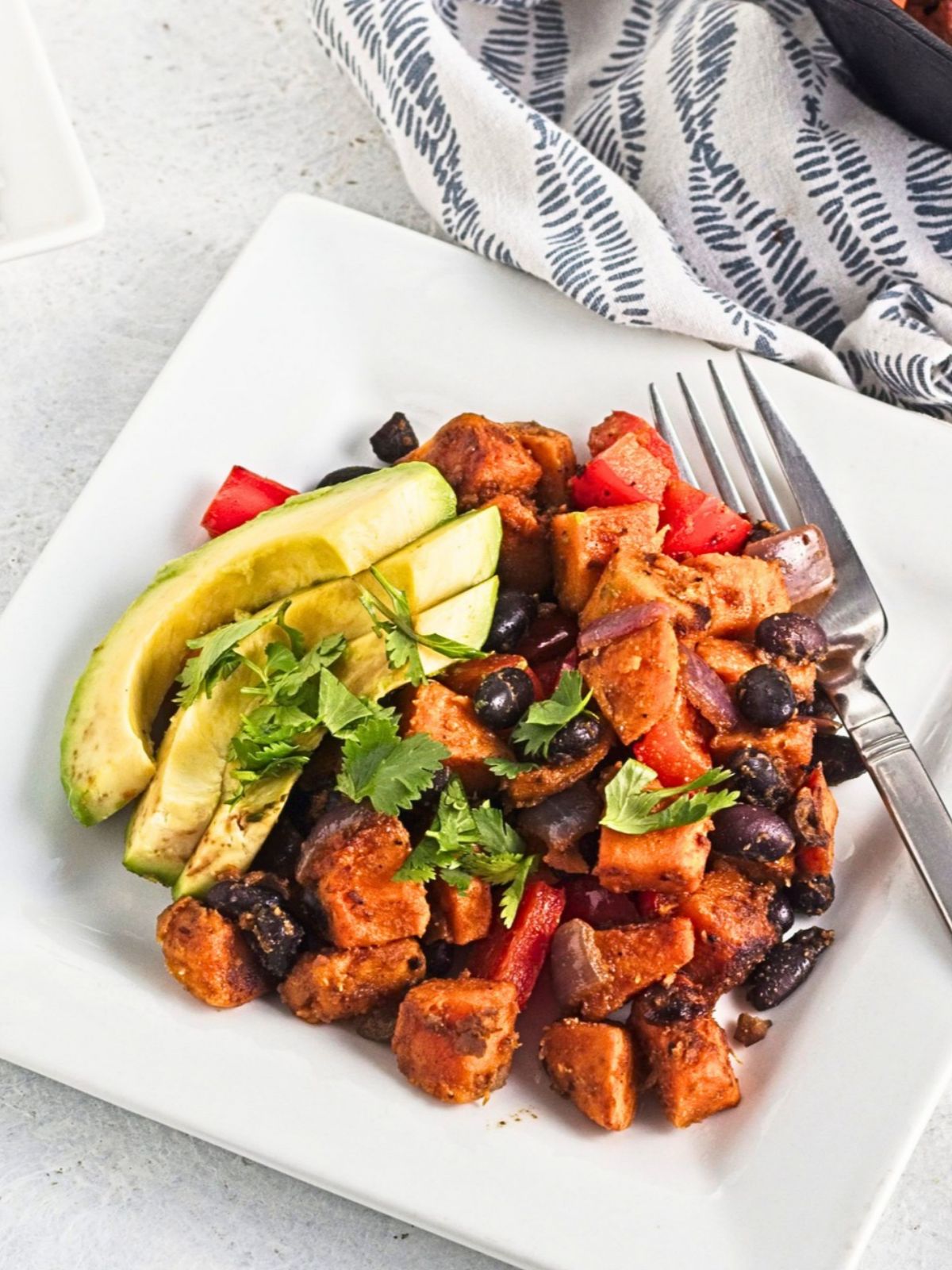 A serving of hash topped with sliced avocado and fresh cilantro on a white plate.