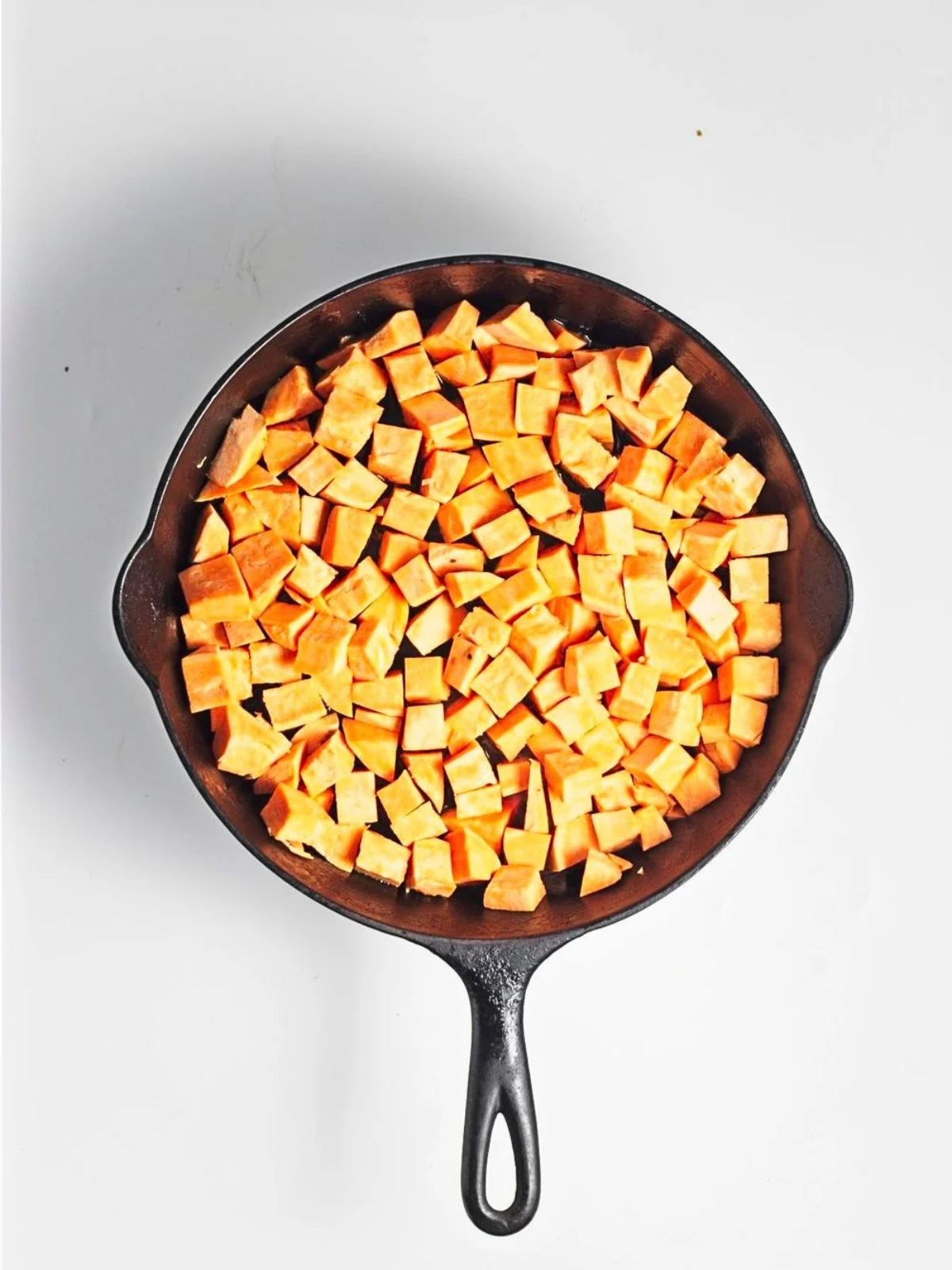Diced sweet potatoes arranged in a single layer in a cast iron skillet before cooking.