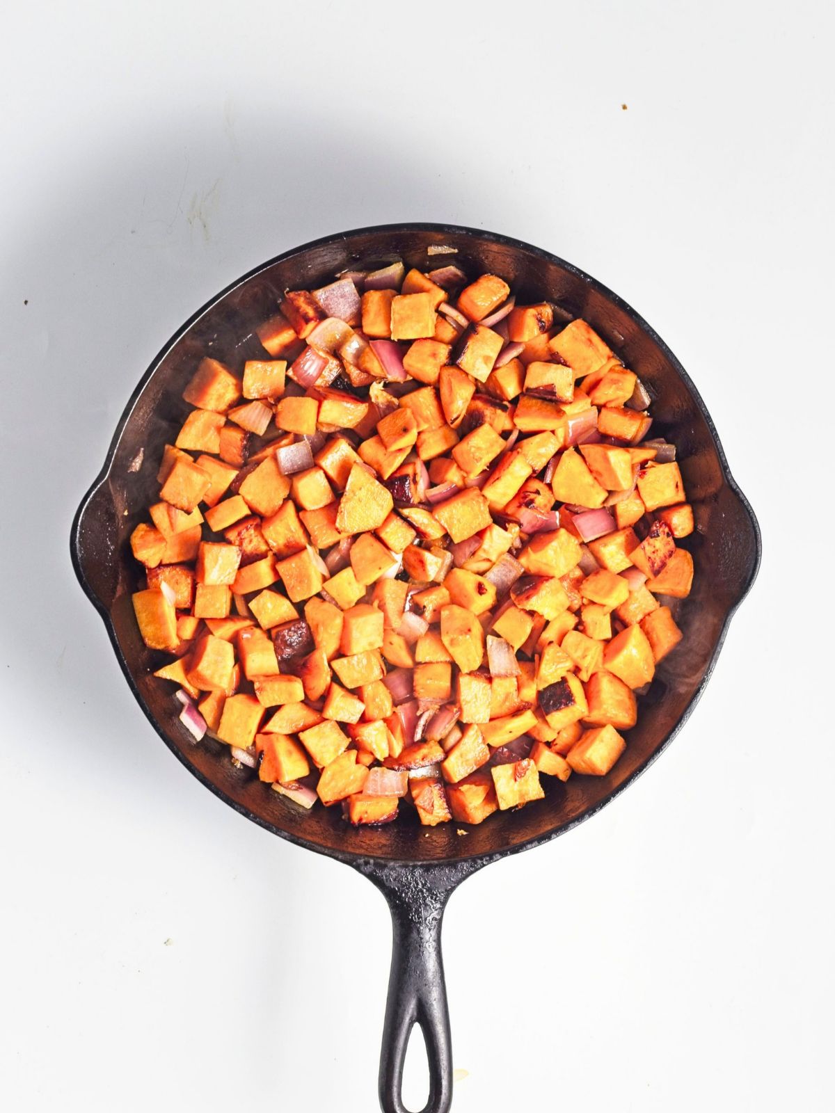 Potatoes and onion cooking together in a cast iron skillet until tender and lightly browned.