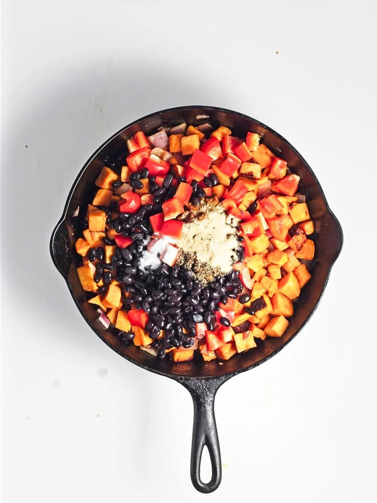 Cooked potatoes and onion in a cast iron skillet with black beans, diced red bell pepper, and seasonings added.