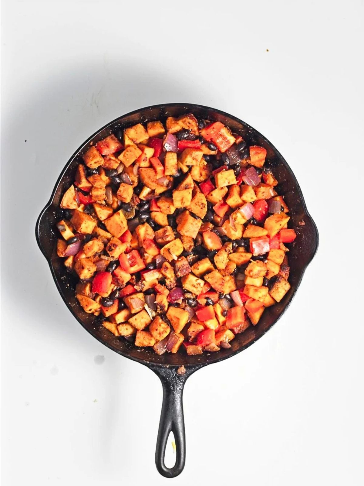Finished sweet potato black bean hash tossed together in a cast iron skillet with browned sweet potatoes, black beans, red bell peppers, red onion, and savory seasonings.