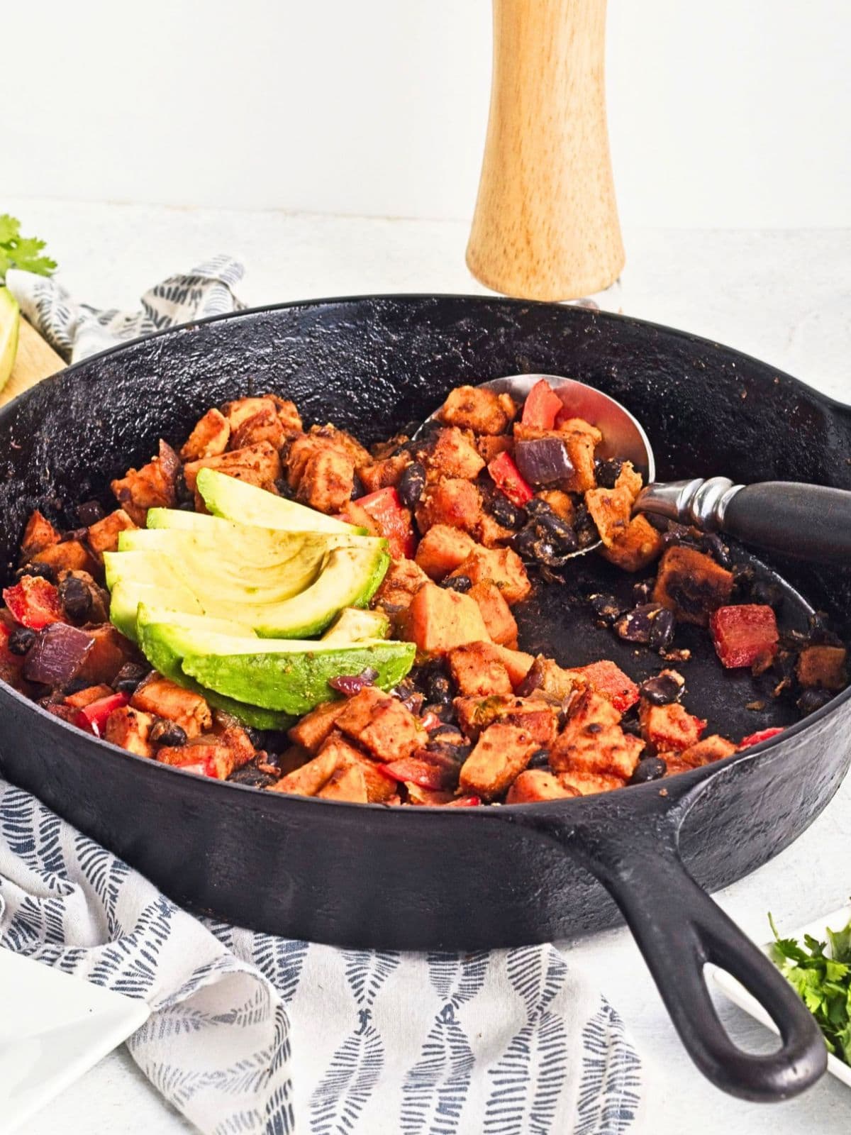Close up of cooked hash in a cast iron skillet with browned sweet potatoes, black beans, red bell peppers, red onion, and savory seasonings.
